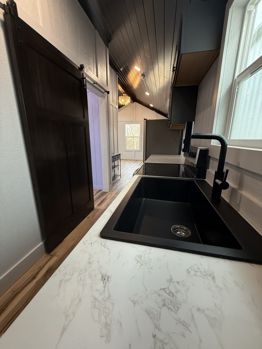 Farmhouse kitchen sink with marble-styled counters and dark barn door in Barn Brothers tiny home