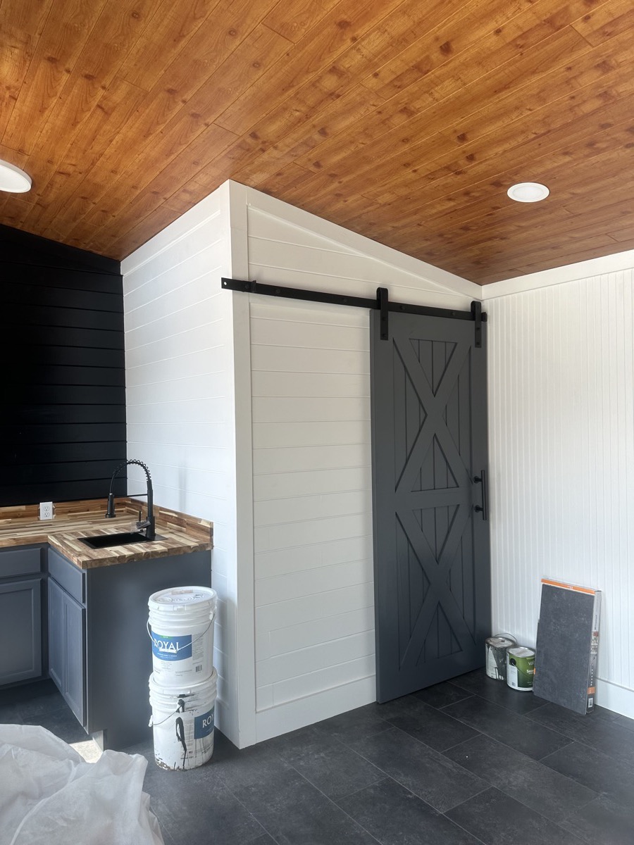 Gray sliding barn door with black hardware and white shiplap walls